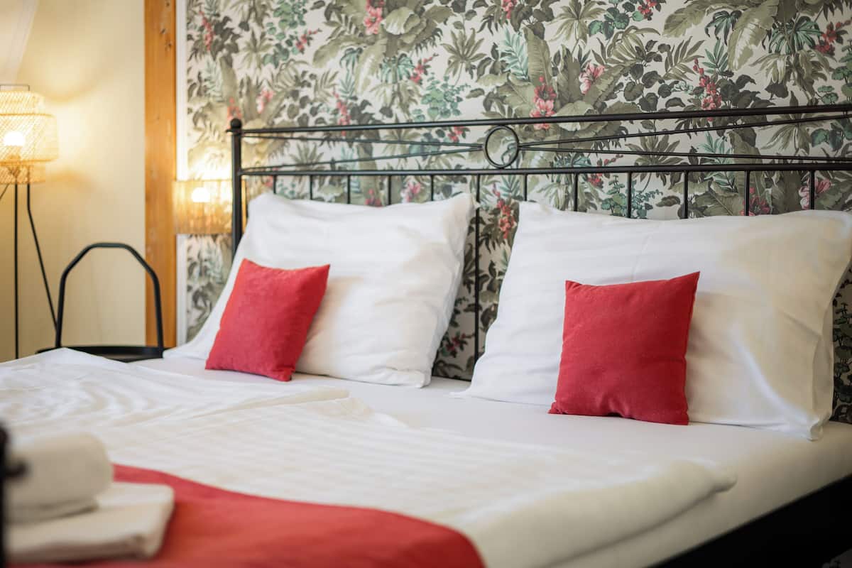 Un lit bien fait, avec des oreillers blancs et rouges, un plaid rouge et un papier peint à motifs floraux.