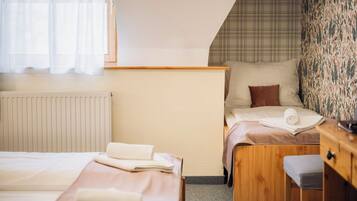 A hotel room with two beds, a wooden desk, a radiator, and a window with sheer curtains.