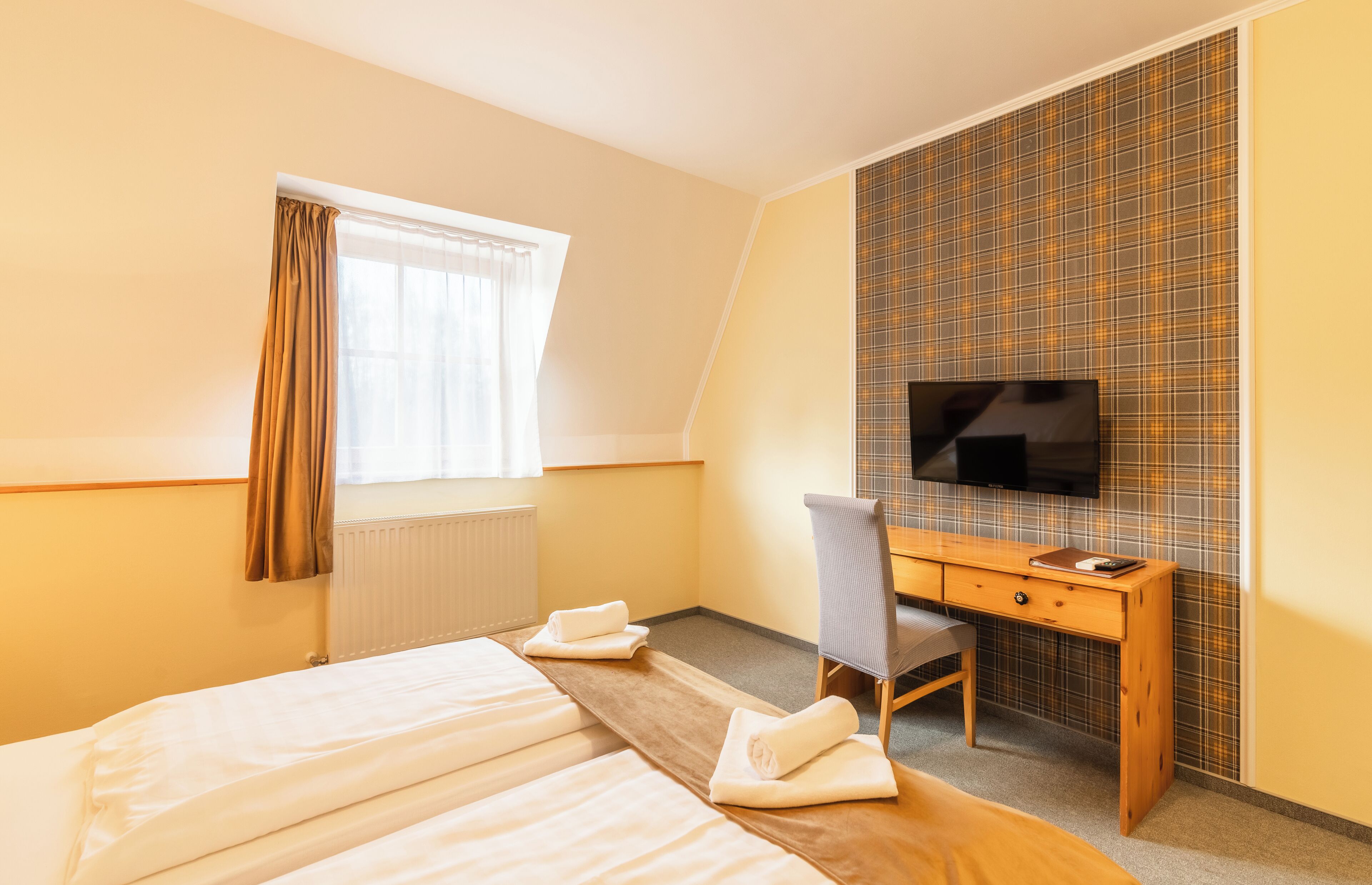 Habitación de hotel con cama, escritorio, silla, televisión y ventana con cortinas.