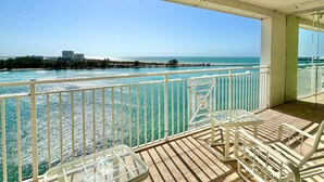 A balcony with a view of the ocean, a white railing, and two chairs.