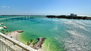 A coastal view with a bridge, clear turquoise water, and a beach with palm trees.