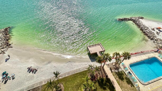A beach with clear turquoise water, a pool, and a small building.