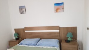 Ein ordentlich bezogenes Bett mit einem hölzernen Kopfteil, zwei Nachttische mit Lampen und zwei an der Wand hängende Bilder.