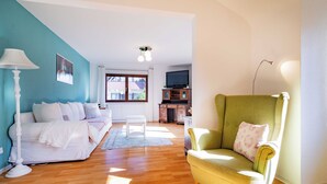 Una sala de estar con un sofá blanco, un sillón verde, una lámpara blanca y un televisor sobre un mueble de madera.