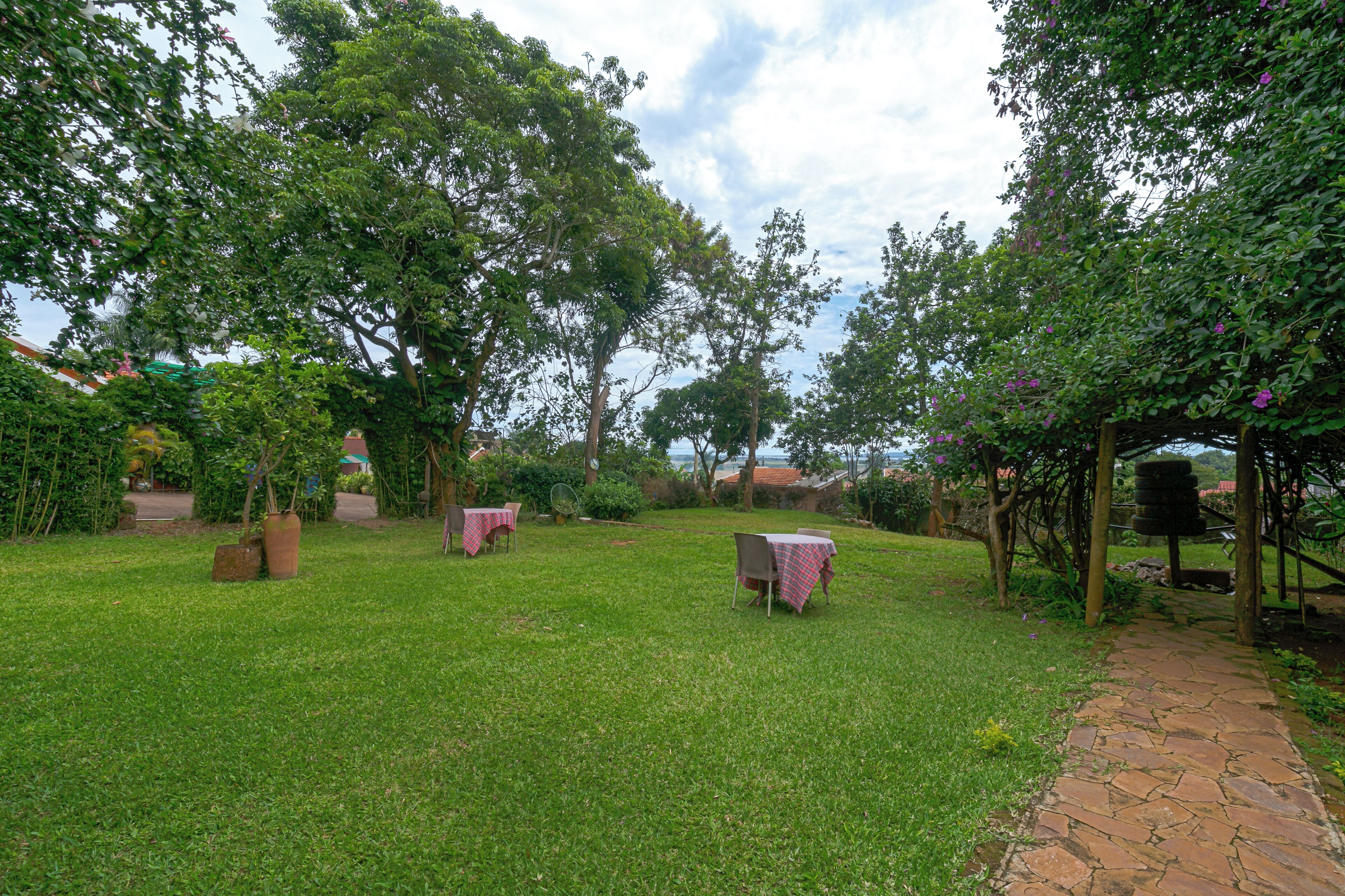 Un jardin avec un chemin pavé, des tables recouvertes de nappes roses et une végétation luxuriante.
