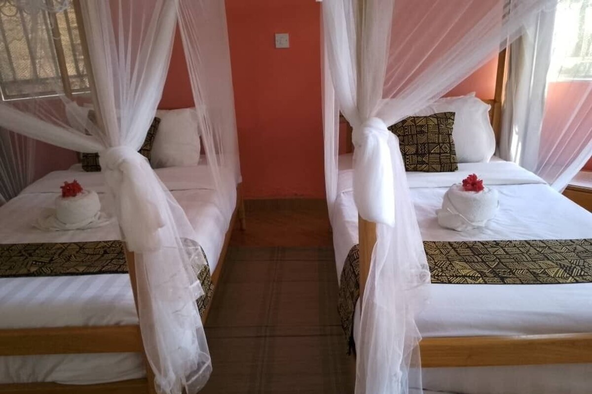 Twee enkele bedden met witte lakens en decoratieve spreien, elk met een hemelbed en een sierkussen.