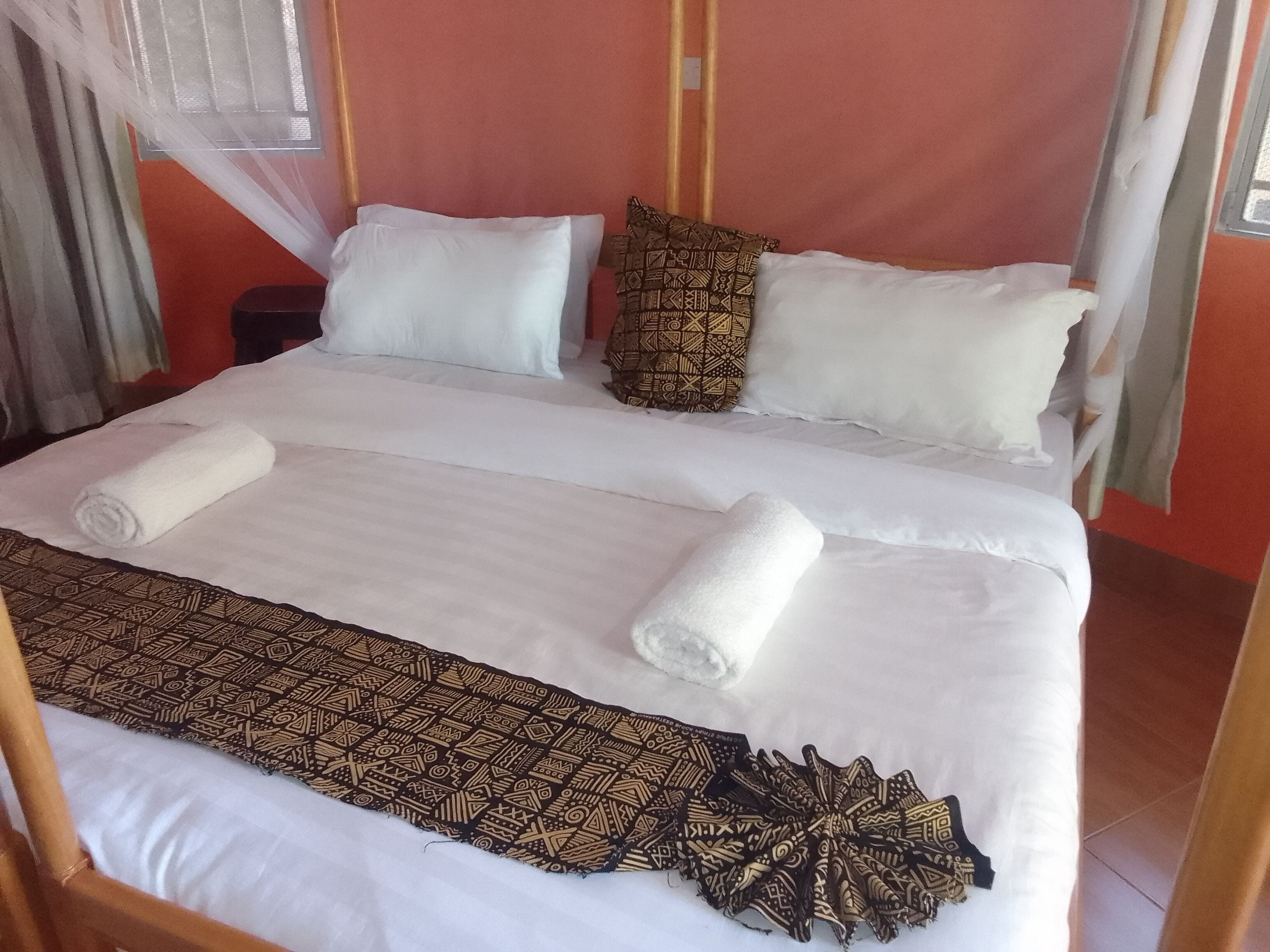 Cama com roupa de cama branca, manta estampada e duas almofadas com designs diferentes.