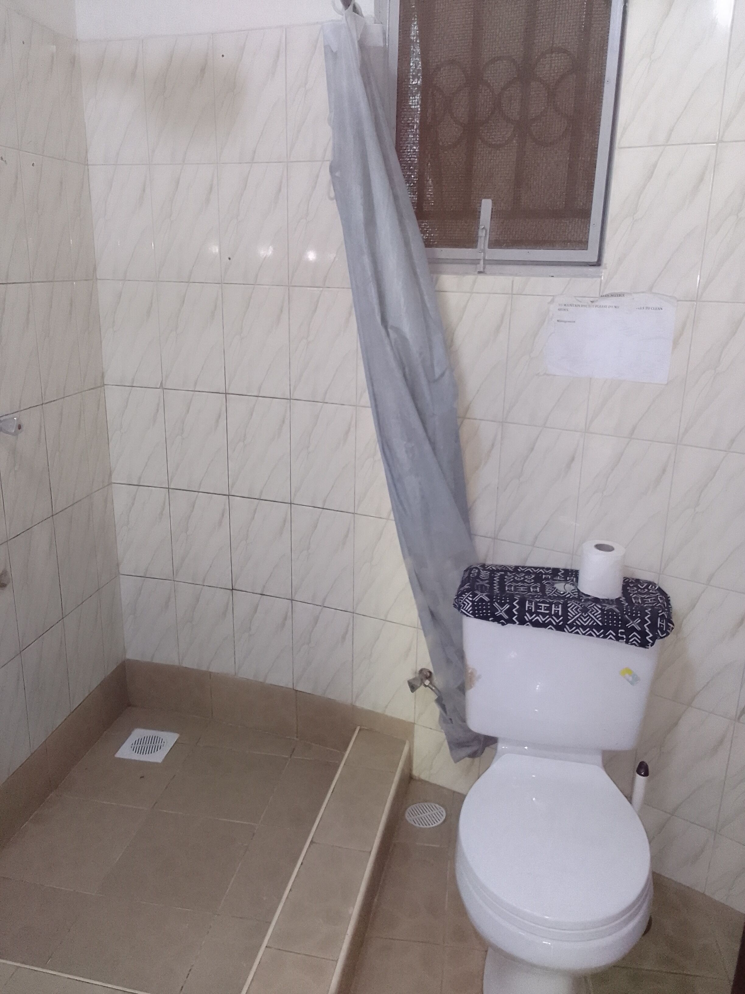 Une salle de bain comprenant des toilettes, un espace douche et un sol carrelé.