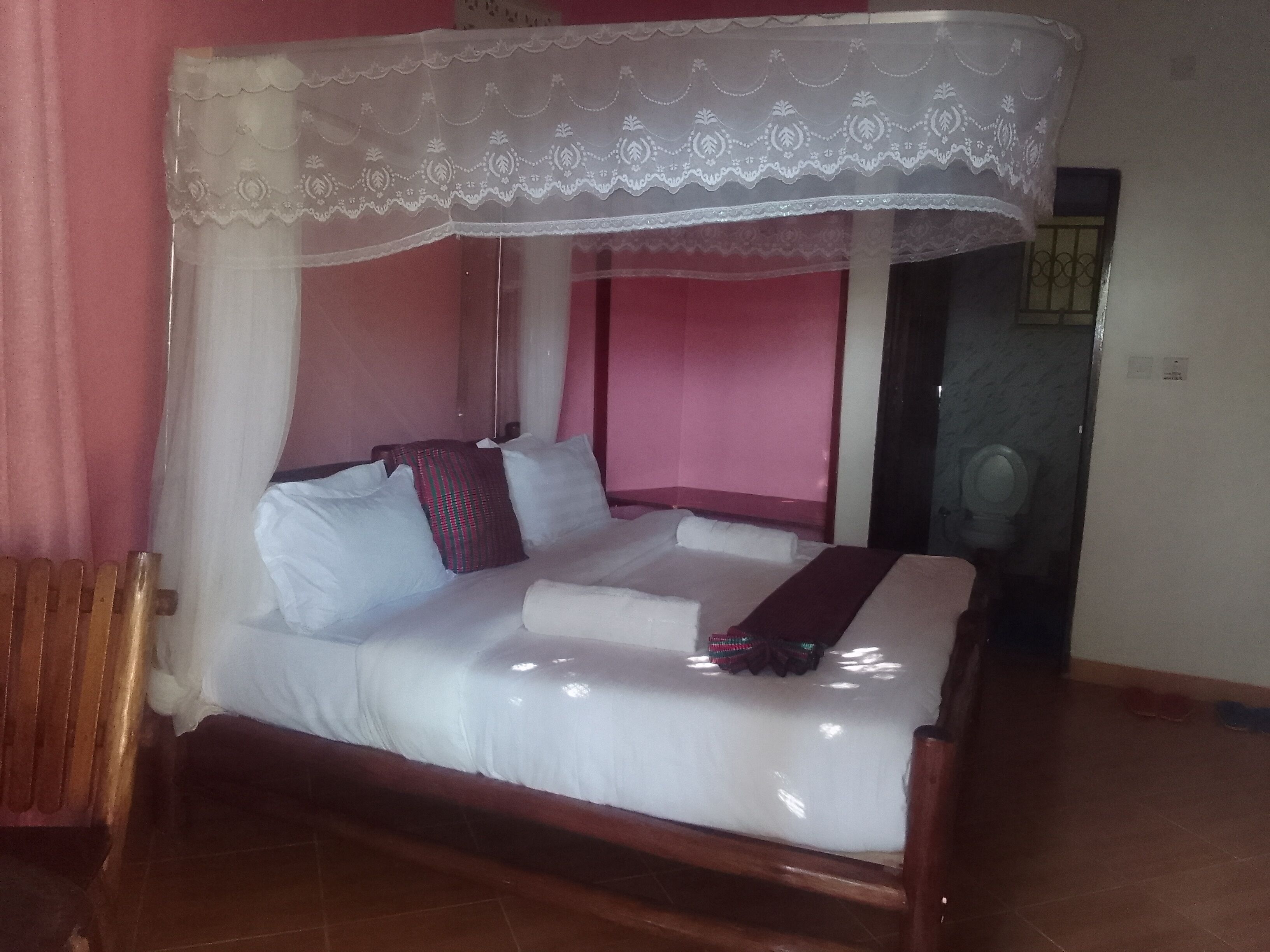A bed with a canopy, a wooden headboard, and a red wall.