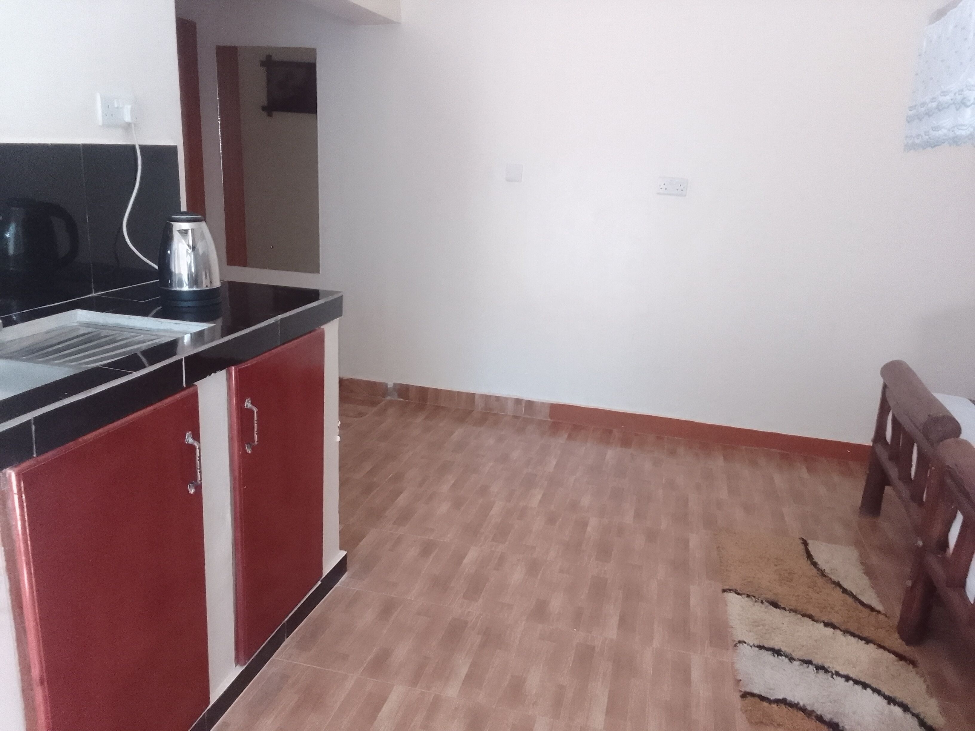 Una cocina con encimera negra, armarios rojos y suelo de madera.