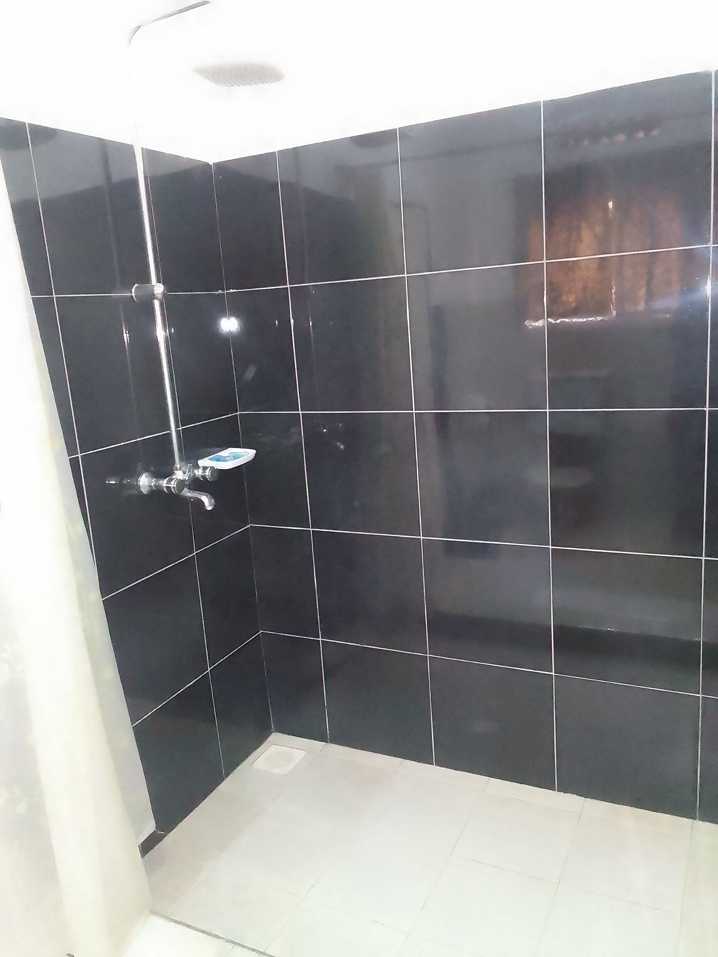 A bathroom with black tiled walls, a white floor, and a shower with a chrome faucet.