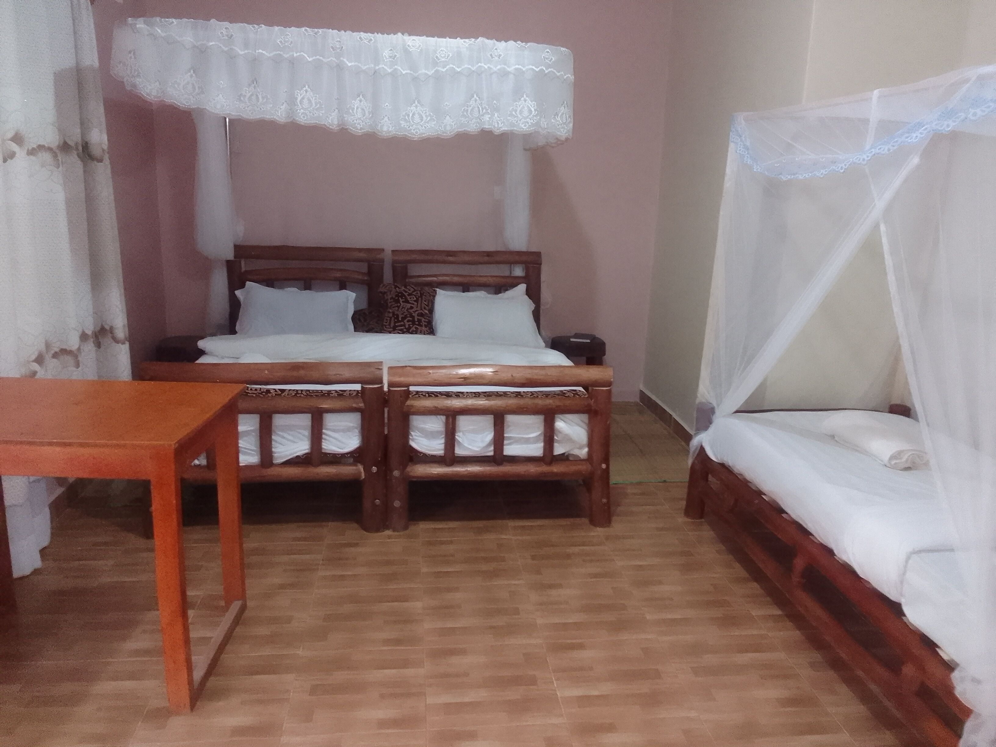 Ein Zimmer mit zwei Holzbetten, davon eines mit Baldachin und eines ohne, einem kleinen Holztisch und einer schlichten Wand.