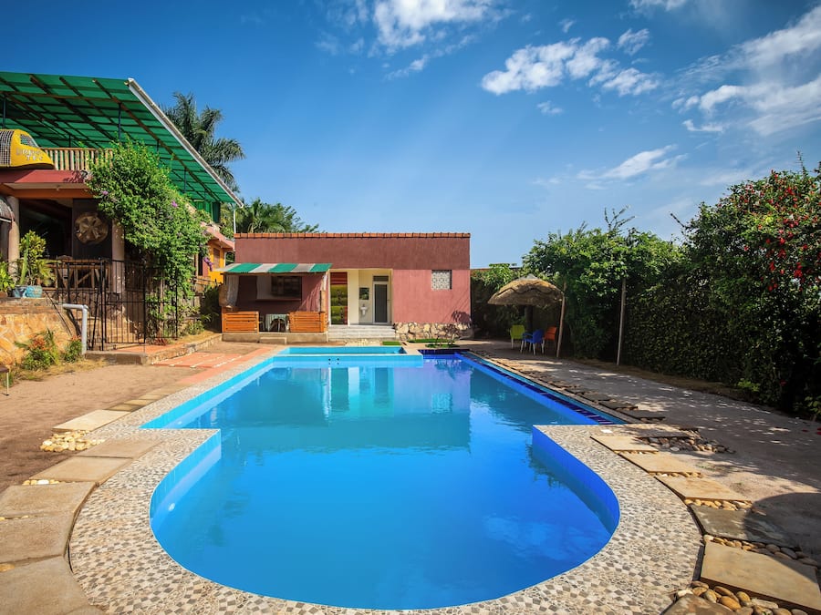 Una piscina con borde de baldosas, un pequeño edificio con techo rojo y un toldo verde.