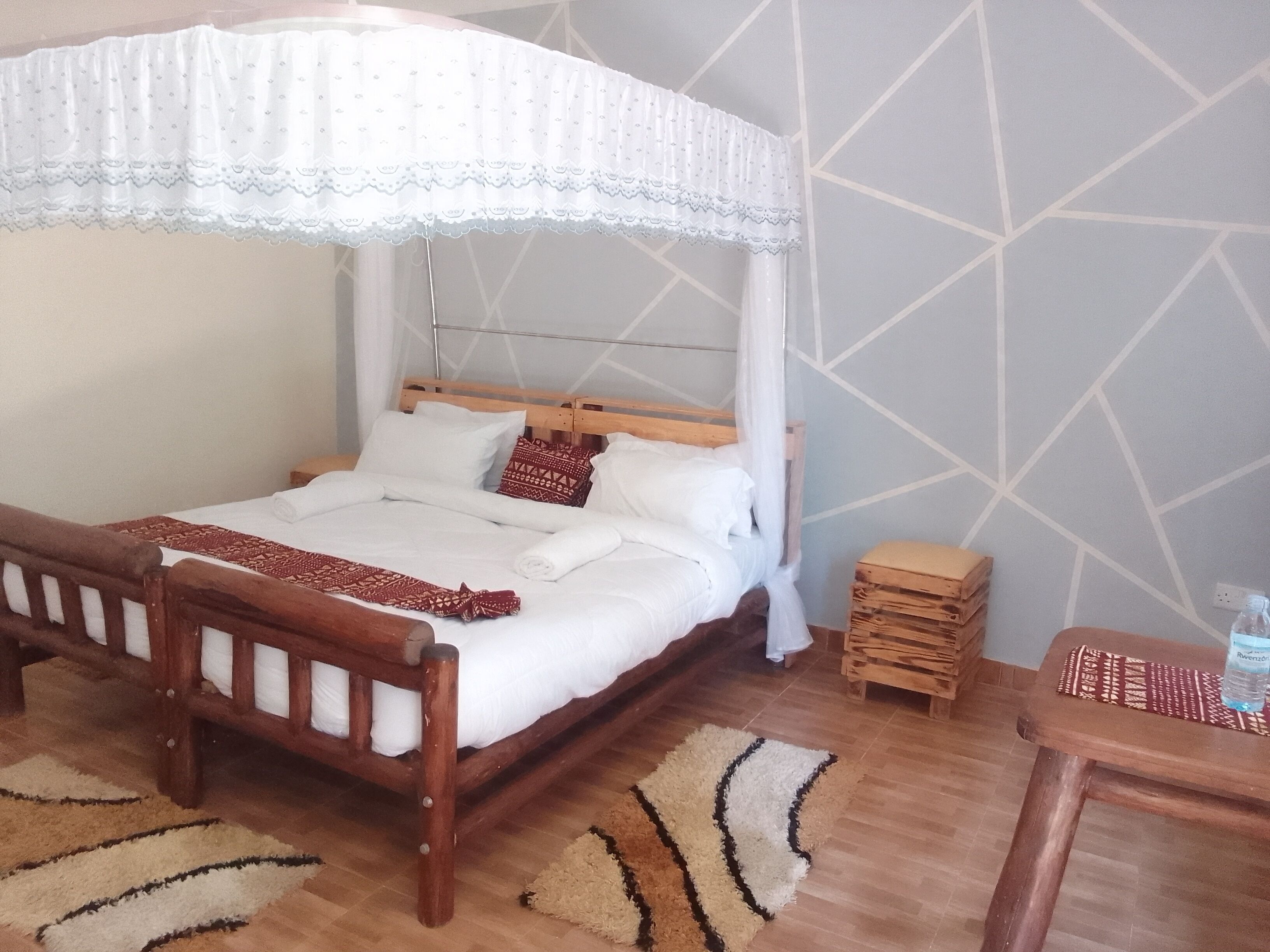 Een slaapkamer met een houten bed, wit beddengoed, een baldakijn, een klein houten nachtkastje en een vloerkleed met een patroon.