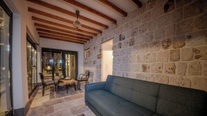 Una sala de estar acogedora con pared de piedra, vigas de madera, un sofá azul y un comedor con mesa y sillas.