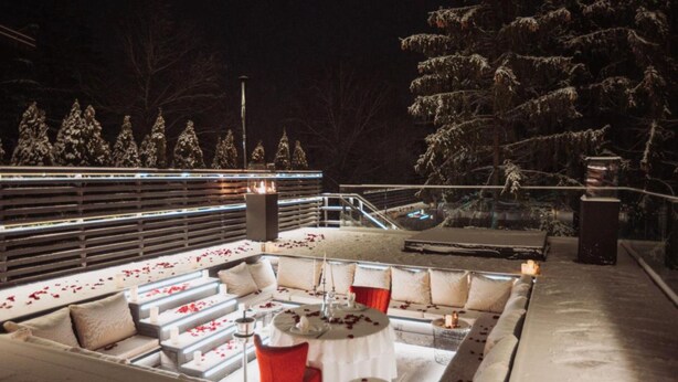 An outdoor seating area with tables and chairs, surrounded by snow-covered trees and a railing. - Alpin Aparthotel 2302 (Brasov)