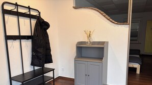A room with a coat rack, a grey cabinet, a small shelf with a vase, and a wooden bench. - Cozy apartment with kitchen and good transport connections (Spremberg)