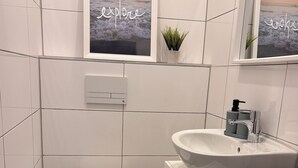 A modern bathroom with a toilet, sink, and a small window with a view of the ocean. - Cozy apartment with kitchen and good transport connections (Spremberg)