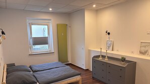 A bedroom with two beds, a dresser, a window with blinds, and a radiator. - Cozy apartment with kitchen and good transport connections (Spremberg)