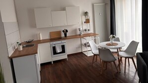 A modern kitchen with white cabinets, a wooden countertop, and a built-in oven. There is a dining area with a round table and white chairs. - Cozy apartment with kitchen and good transport connections (Spremberg)