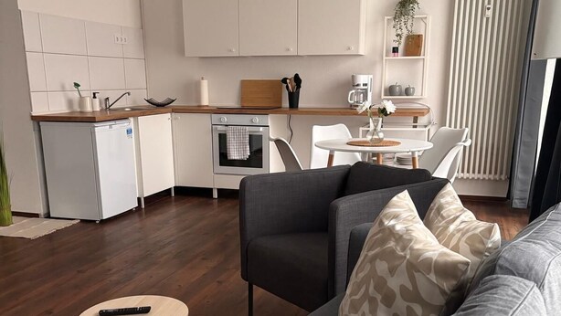 A modern living room with a grey sofa, a small round coffee table, and a kitchen area in the background. - Cozy apartment with kitchen and good transport connections (Spremberg)