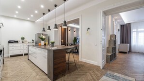 A modern kitchen with a central island, pendant lighting, and a herringbone wooden floor. - The Prestige L’Or Suite 4-BDR with two balcony (Budapest)