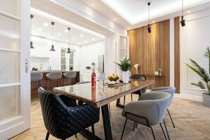A modern kitchen with white cabinets, a wooden accent wall, and a dining area with a glass table and leather chairs. - The Prestige L’Or Suite 4-BDR with two balcony (Budapest)