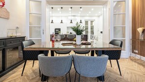 A modern dining area with a glass-top table, four grey chairs, and pendant lighting. - The Prestige L’Or Suite 4-BDR with two balcony (Budapest)