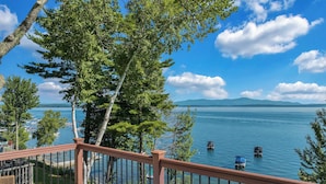 A deck with a view of a lake, boats, and distant mountains. - Lakefront, Mtn Views, Hot Tub, Game Room, & More! (Gilford)