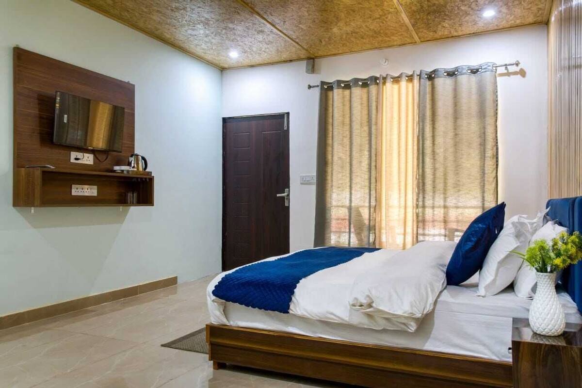 A bedroom with a bed, a TV mounted on the wall, a door, and a window with curtains.