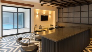 A modern kitchen with a central island, bar stools, a large window, and a flat-screen TV mounted on the wall.