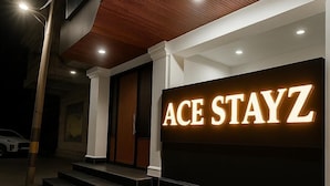 A hotel entrance with a large illuminated sign reading "ACE STAYZ" and a set of steps leading up to the door.
