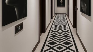 A hallway with a geometric patterned floor, framed artwork on the walls, and a door with the number 171.
