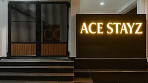A hotel entrance with a prominent illuminated sign reading "ACE STAYZ" and a set of dark wooden steps leading up to the door.