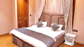 A bedroom with a bed, curtains, a nightstand, and a wooden door.