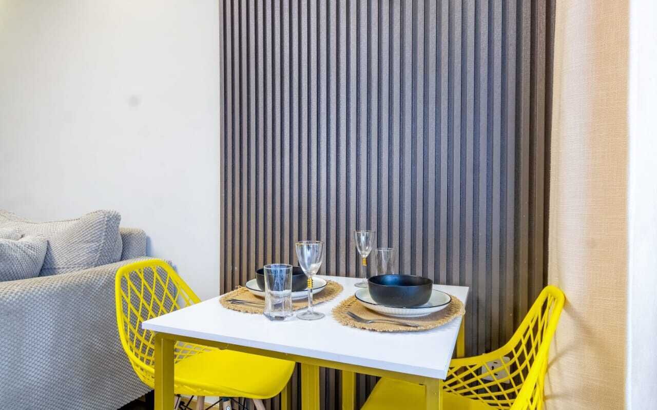 Ein Essbereich mit einem weißen Tisch, gelben Stühlen und einer vertikal gestreiften Wand.