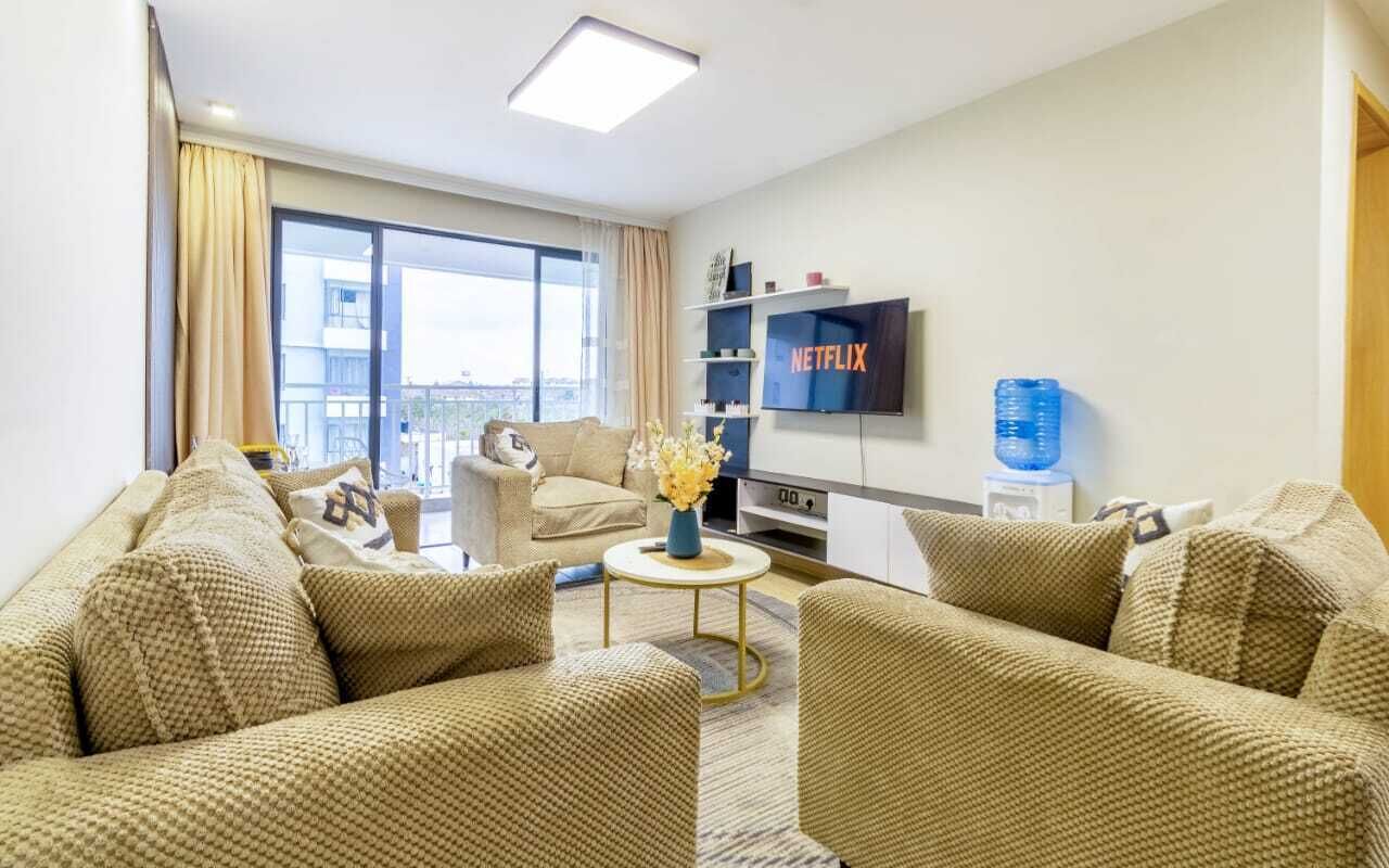 Una sala de estar moderna con un conjunto de sofá, una mesa de centro, un televisor de pantalla plana y un ventanal con cortinas.