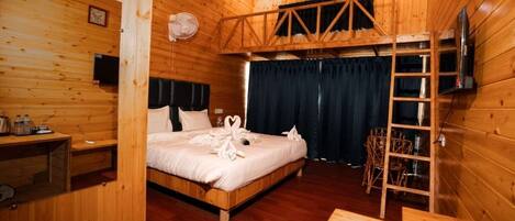A wooden cabin room with a bed, a desk, a chair, and a ladder.