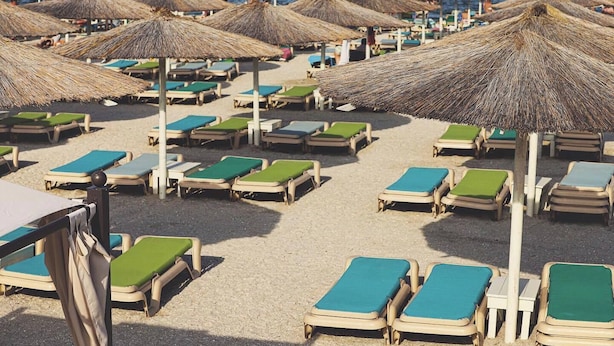 Une plage bordée de rangées de chaises longues et d’ombrelles en chaume.