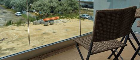 Un balcon avec un fauteuil en osier, une vue sur un chantier de construction et un immeuble en arrière-plan.