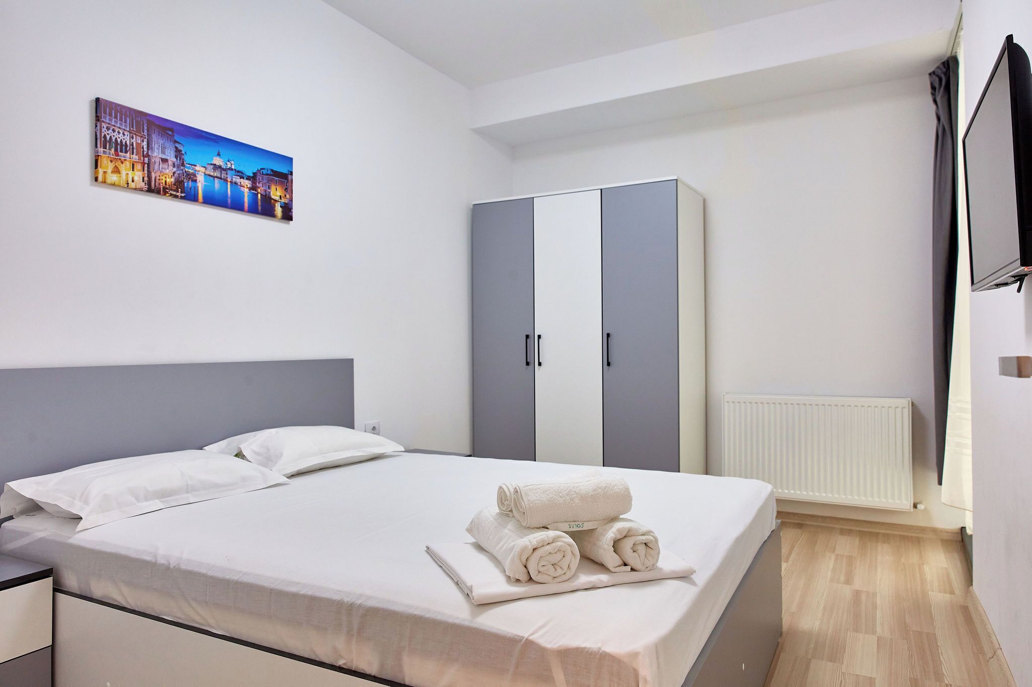 A hotel room with a bed, a wardrobe, a painting on the wall, and a television.