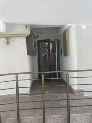 Escadaria que leva a um espaço interior, com corrimão de metal e uma porta com uma placa em cima.