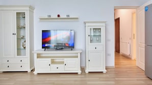 Un salon avec un téléviseur à écran plat posé sur un meuble blanc, flanqué de deux armoires blanches dotées de portes en verre.