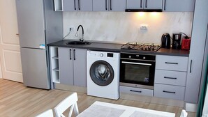 Une cuisine compacte avec des meubles gris, un réfrigérateur en acier inoxydable, un lave-linge et une cuisinière.