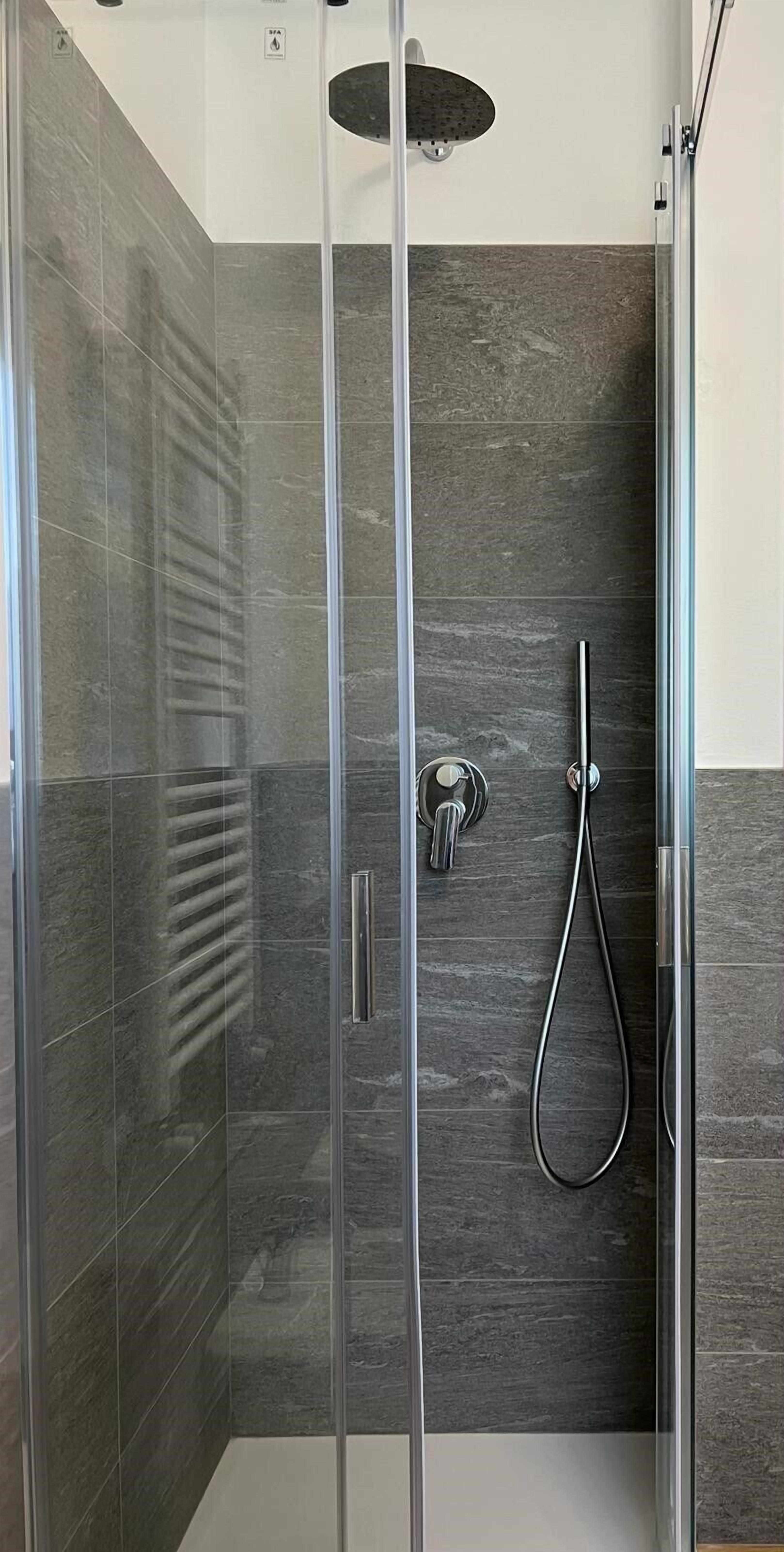 Una ducha moderna con puerta de vidrio, cabezal de ducha de mano y grifo empotrado.