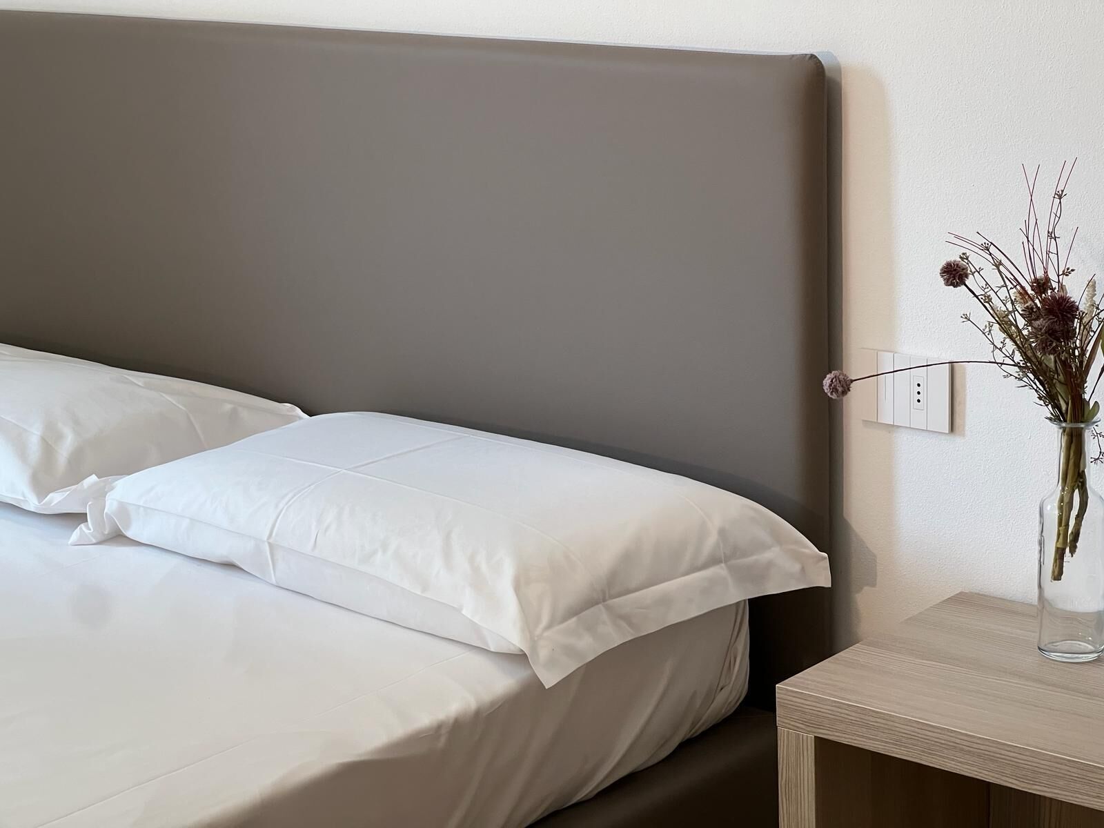 A neatly made bed with white linens and a grey headboard.