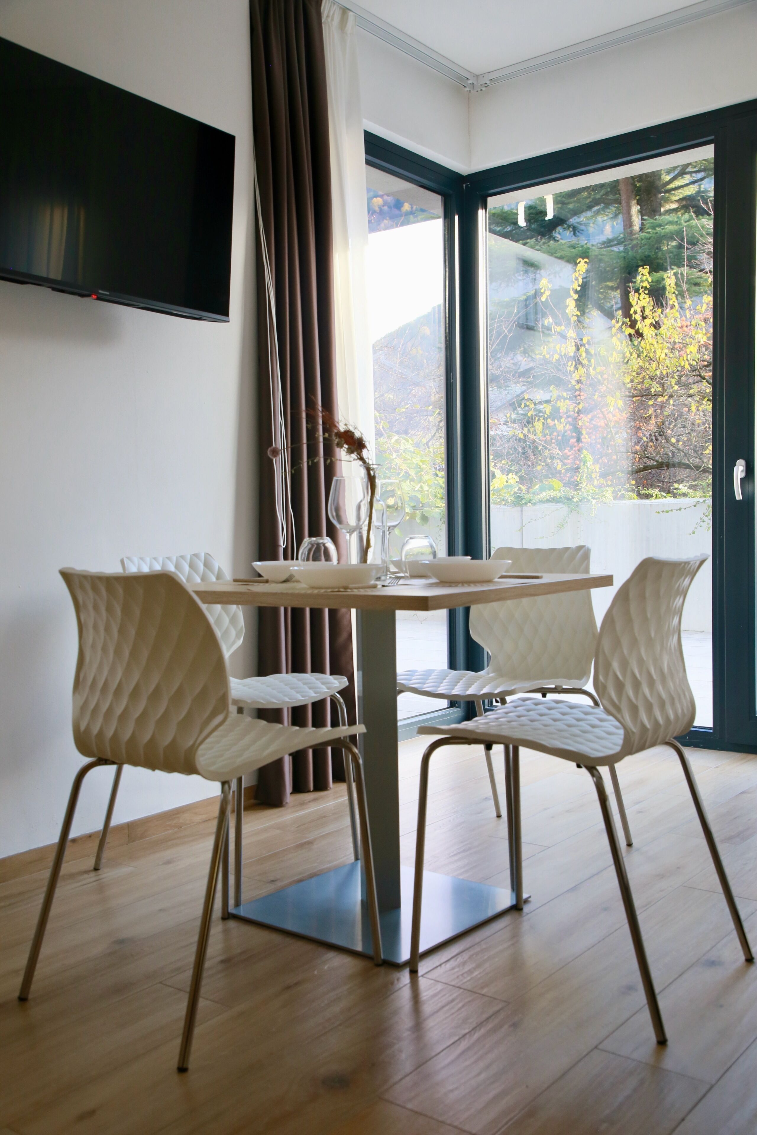 Un comedor con una mesa, sillas, un televisor y vistas a través de un ventanal.