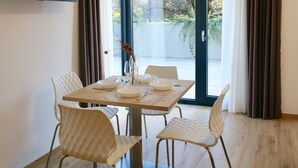 A dining area with a table set for four, two chairs on each side, a flat-screen TV mounted on the wall, and a sliding glass door leading to an outdoor area. - Bernina Suites - 150 metres to Bernina Express (Tirano)