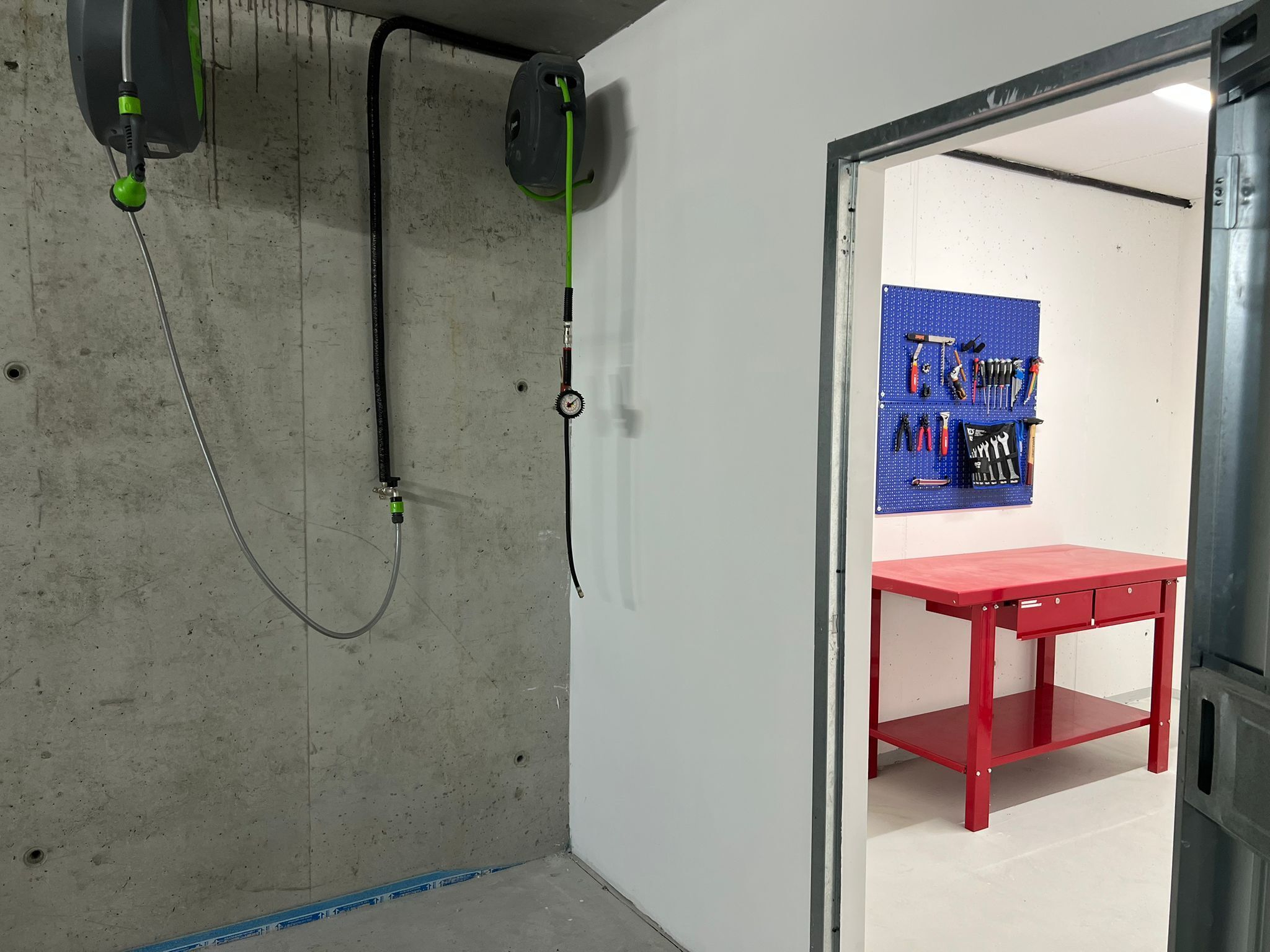 A room with a concrete wall, a red table, and a pegboard with tools.