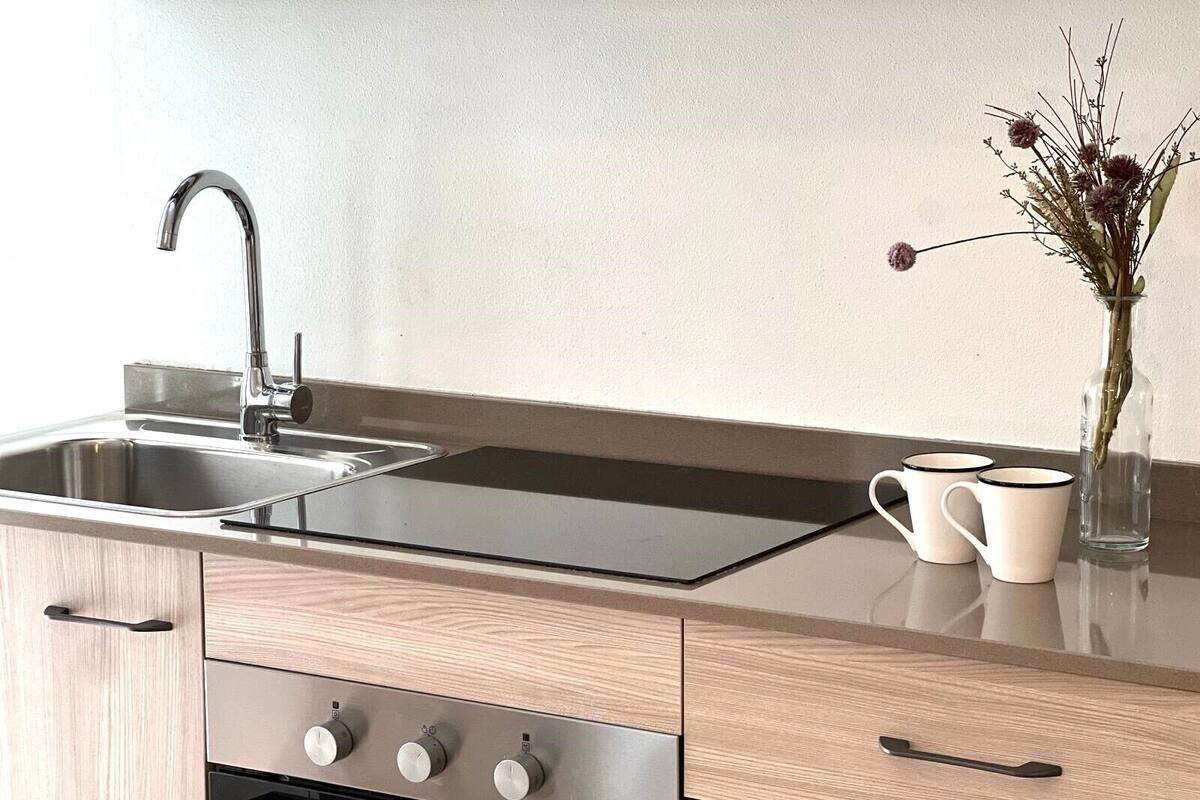 A modern kitchen with a stainless steel sink, a black stovetop, and wooden cabinets.